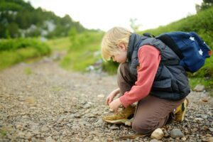 Preteen boy lacing up shoes while tracking on road in mountains valley. Family hiking with kids.