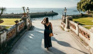 Rear view of woman in long dress walking down stone stairs leading to sea near Miramare in Trieste.