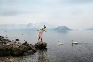 A girl in a pink tulle skirt admires white swans on Lake Como, Italy. Idealistic landscape