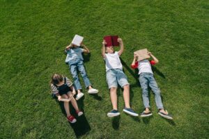 High angle view of cute multiethnic kids reading books on green grass in park