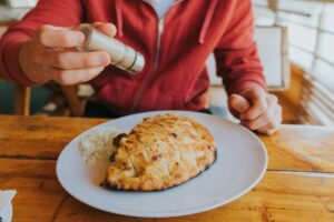 Man adding pepper on a traditional Bosnian dish called cevapi