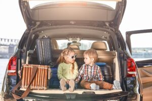 No road is long with good company. Little cute kids in the trunk of a car with suitcases looking at